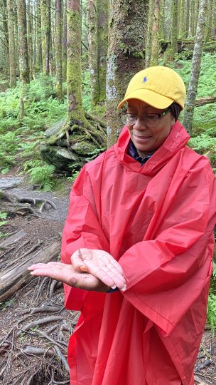 A woman in a rain poncho and hat holds a small salamander in her hands.