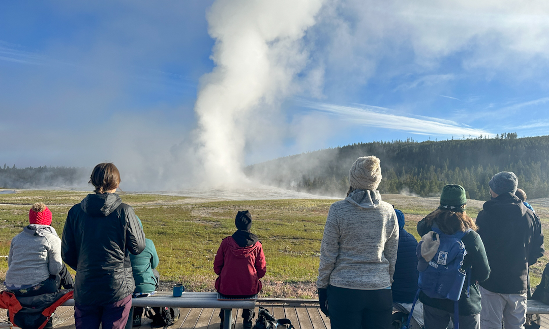 people in front of erupting geyser